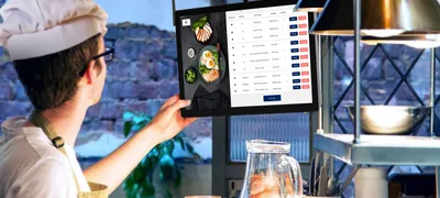 Chef in a commercial kitchen holding a tablet showing a digital checklist